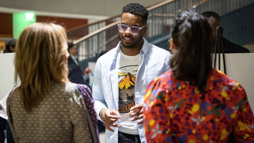 : A young man meets two women in a busy atrium during a Rutgers Law School career development event.
