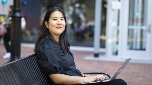 A female student smiles for the camera while sitting on a bench outside Rutgers Law School on a sunny day.