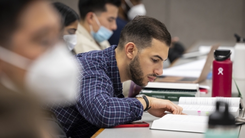 A Rutgers Law Student studies from a textbook in a classroom surrounded by students.