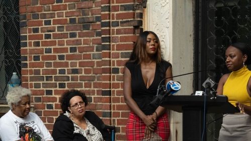 woman at podium speaking into mics during press conference outside apartment building