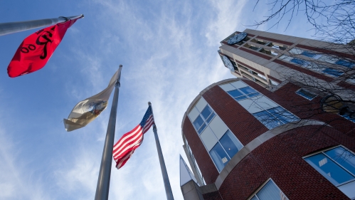 Flags flying in front of Rutgers Law School in front of a blue sky with whispy clouds.