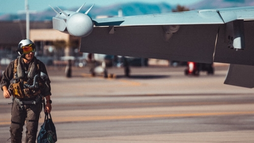 airman in uniform and helmet walking next to fighter plane