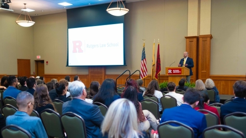 people seated in large room looking forward to man speaking at podium