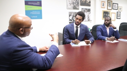 Three men in blue suits seated at conference room table