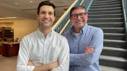 two men posing for a photograph in front of stairs