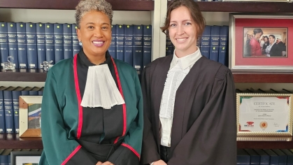 Two women in judicial robes standing next to each other and smiling in front of bookcase