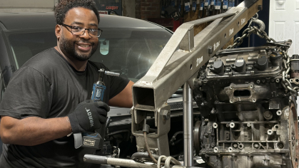man smiling in all black working on machine in auto garage