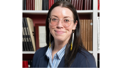 woman with long dark hair wearing glasses smiling in front of bookcase