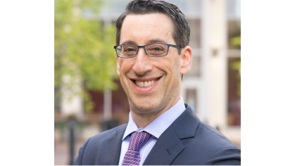 man smiling wearing glasses and business suit outdoors