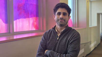 man with arms folded smiling next to colorful window