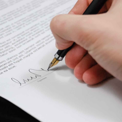 Hand holding pen and signing signature onto white paper