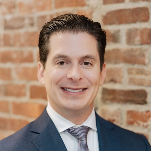 Man in blue suit smiling in front of brick wall