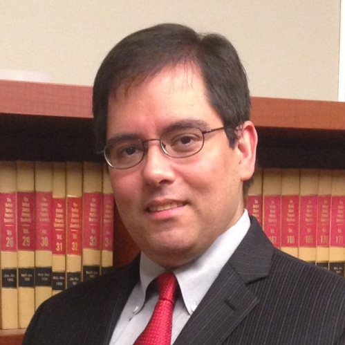 man in glasses and suit smiling in front of bookcase