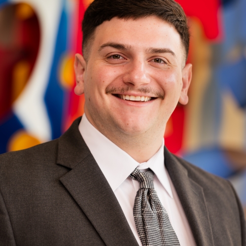 man smiling in suit and tie in front of colorful mural
