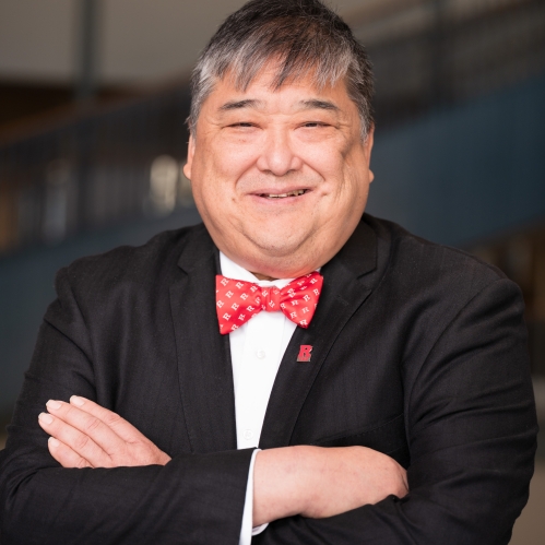 man in black blazer, white shirt, and red bowtie smiling with arms folded