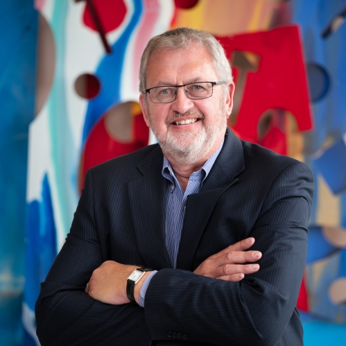 man wearing glasses smiling with arms crossed in front of colorful art