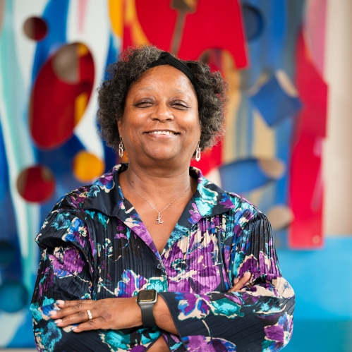 woman in colorful blouse smiling with arms folded in front of art