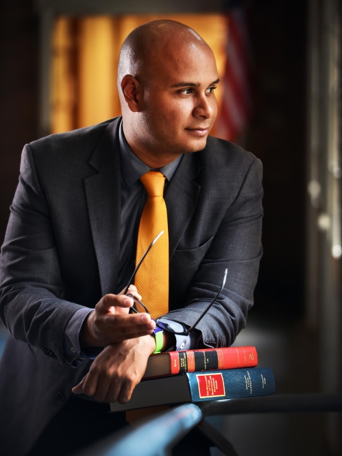 Man looking to the side with his arms on a stack of textbooks holding glasses
