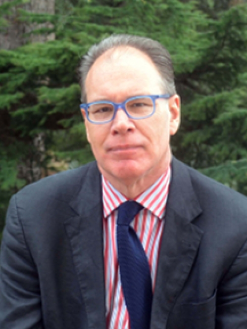 Man grinning wearing glasses, a pink and white striped shirt, blue tie, and suit jacket