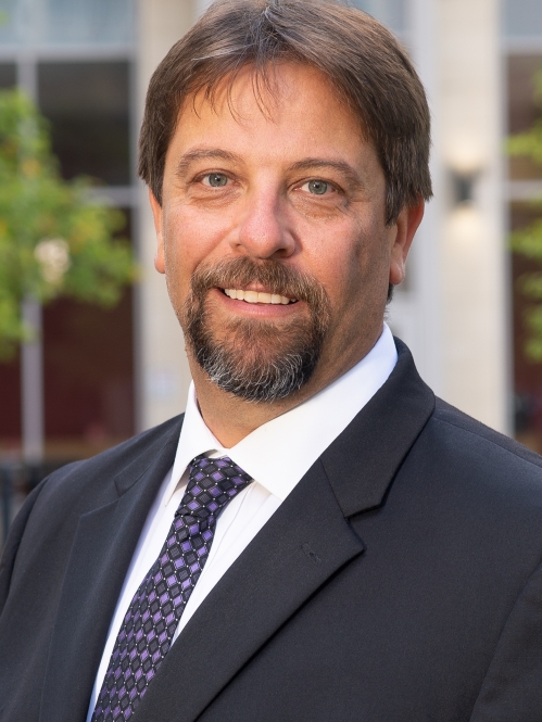 Man grinning wearing white button down shirt, blue tie, and suit jacket