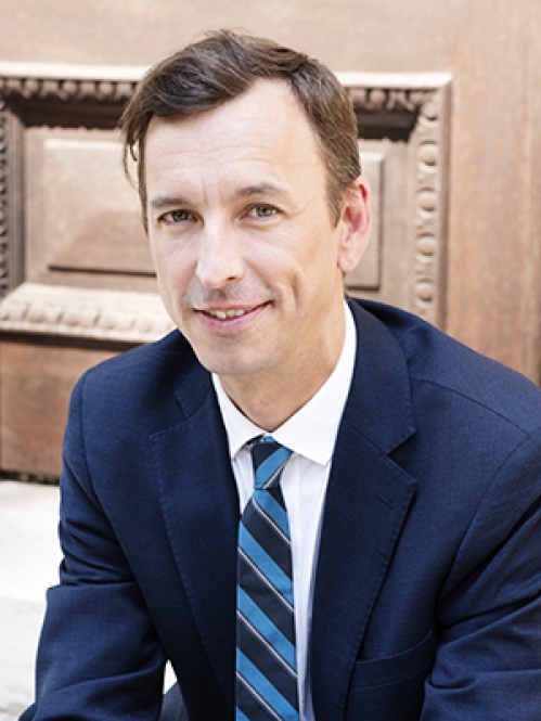Man in blue suit smiling and sitting on stairs in front of building