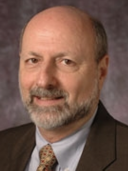 Man smiling wearing dark colored suit and amber tie. 