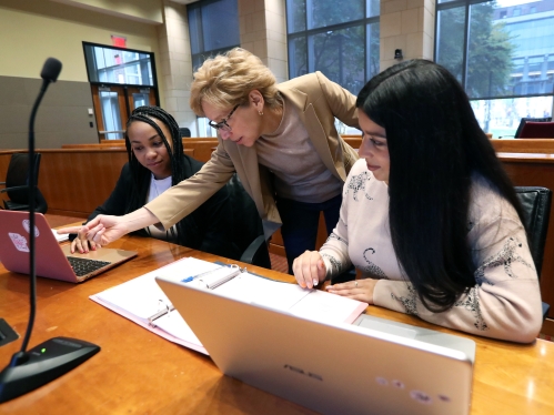 Professor pointing to laptop between two students in mock courtroom