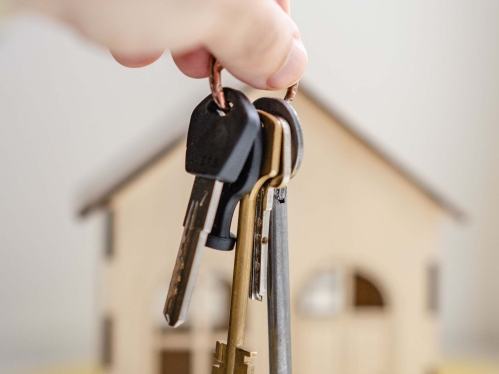 Hands dangling set of keys in front of small toy house