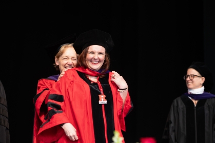woman in red robe and black cap being hooded on stage