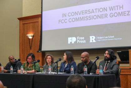 row of men and woman on dais speaking into mics on table