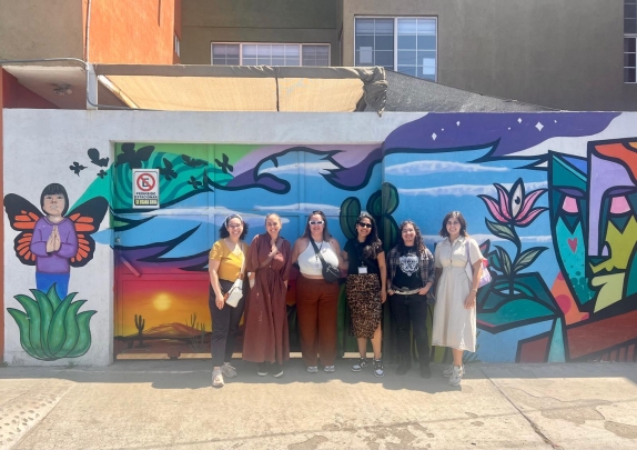group of women standing side by side in front of colorful mural