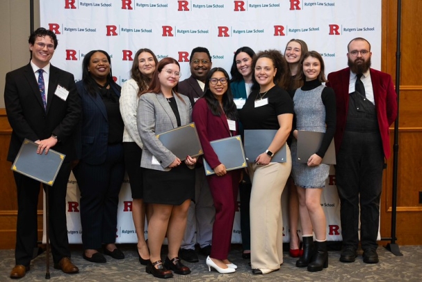 group of men and women smiling and holding certificates in front Rutgers Law School backdrop