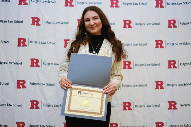 woman with long hair smiling and holding certificate in front of Rutgers Law School background