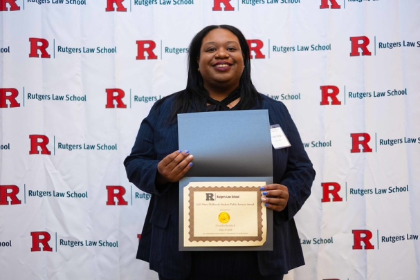 woman holding certificate and smiling in front of Rutgers Law School background