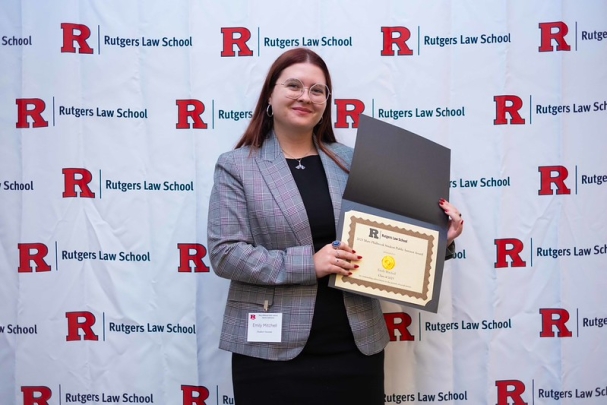 woman holding certificate and smiling in front of Rutgers Law School background
