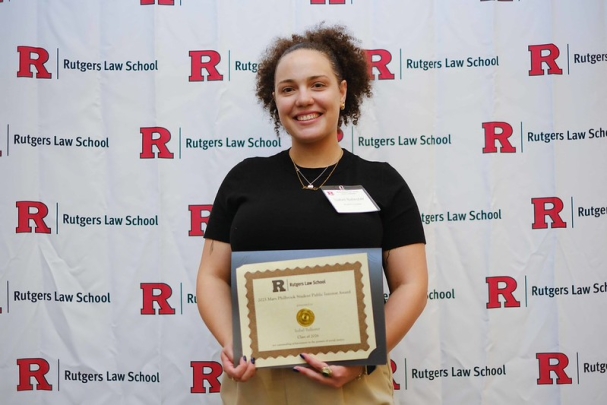 woman smiling and holding certificate in front of Rutgers Law School background