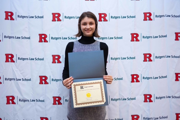 woman holding certificate and smiling in front of Rutgers Law School background