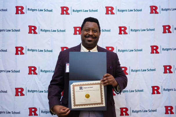 man smiling and holding certificate in front of Rutgers Law School background