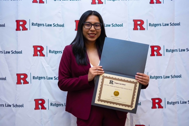 woman holding certificate and smiling in front of Rutgers Law School background