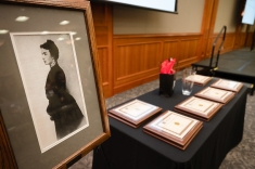 black and white framed photo of woman dressed in Victorian attire next to table of plaques