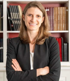 woman with arms folded smiling in front of bookshelves