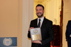 man in suit and tie smiling and holding plaque