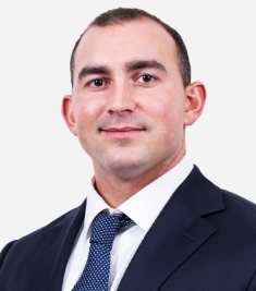 man in dark suit and blue tie grinning