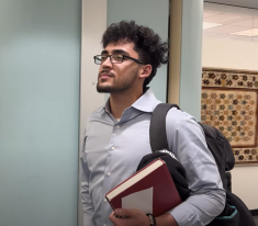 man with glasses holding books and wearing backpack