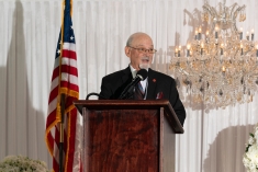man wearing glasses speaking at lectern with American flag behind him