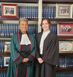Two women in judicial robes standing next to each other and smiling in front of bookcase