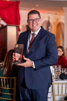 Man in blue suit holding glass plaque in ballroom and smiling