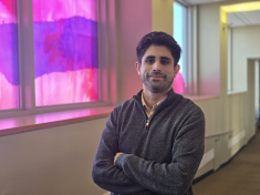 man with arms folded smiling next to colorful window